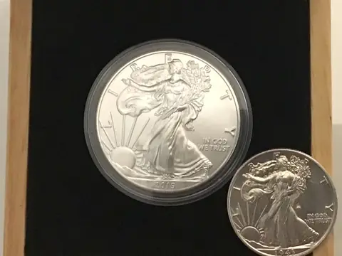 A Silver Eagle in a clear capsule in a wooden box, with a 1943 Walking Liberty half dollar beside it