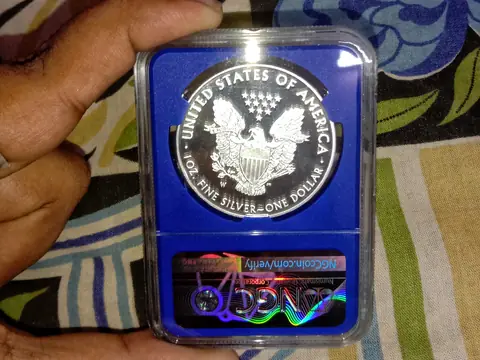A hand holding a 2015 Silver Eagle, eagle side up, in a blue NGC holder