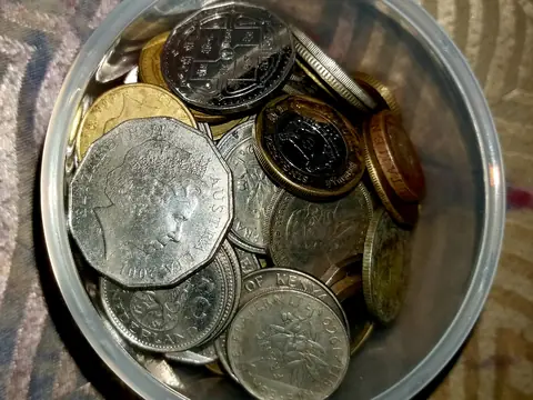 A round plastic tub full of coins from many countries