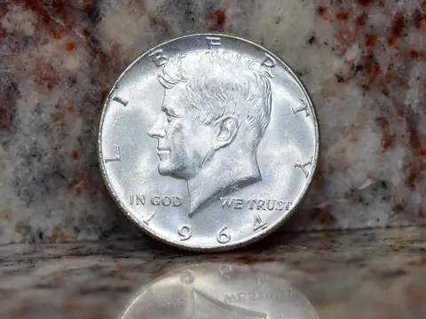 A 1964 Kennedy half dollar standing on a granite counter