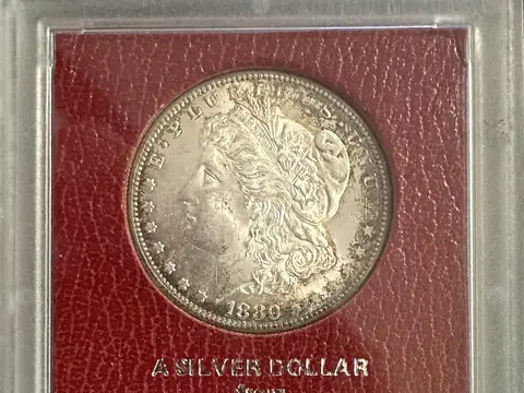 An 1880-S Morgan dollar in a red Paramount holder labelled as from the Redfield collection
