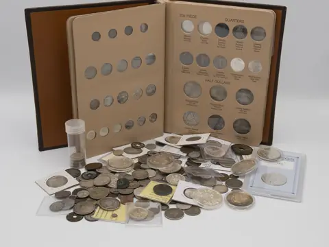 An open coin album of US quarters and half dollars with a tube of coins and a spread of loose coins and coins in flips in front of it
