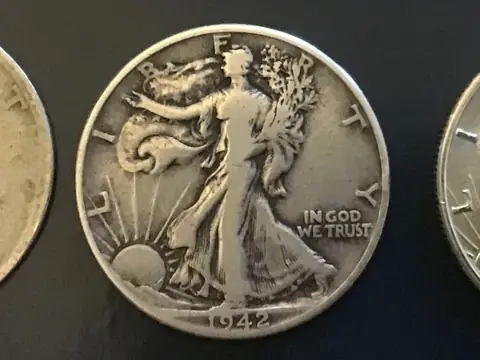 A worn 1942 Walking Liberty half dollar on black, between a coin worn almost smooth and a sharp, nearly uncirculated one