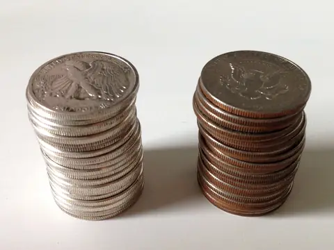 Two stacks of half dollars: silver Walking Liberty halves on the left, later clad halves with copper showing at their edges on the right